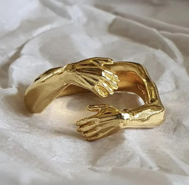 Adjustable geometric love hands embracing ring in gold and silver, perfect for gifts.