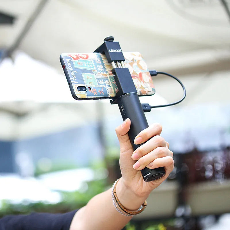Black aluminium alloy portable power bank with an integrated carry handle, shown next to a smartphone for scale.