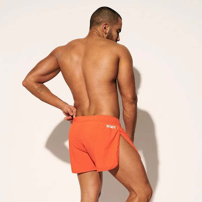 Men's loose orange beach shorts with elastic waist on a sandy shore