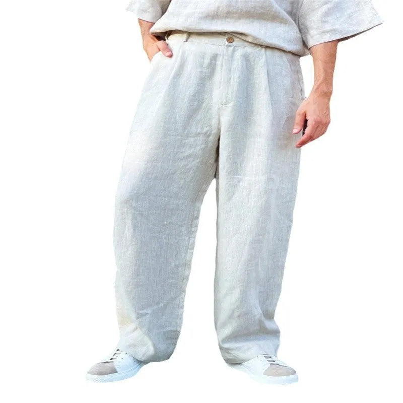 Man wearing loose grey linen blend pleated trousers with a high elasticated waist and straight leg.