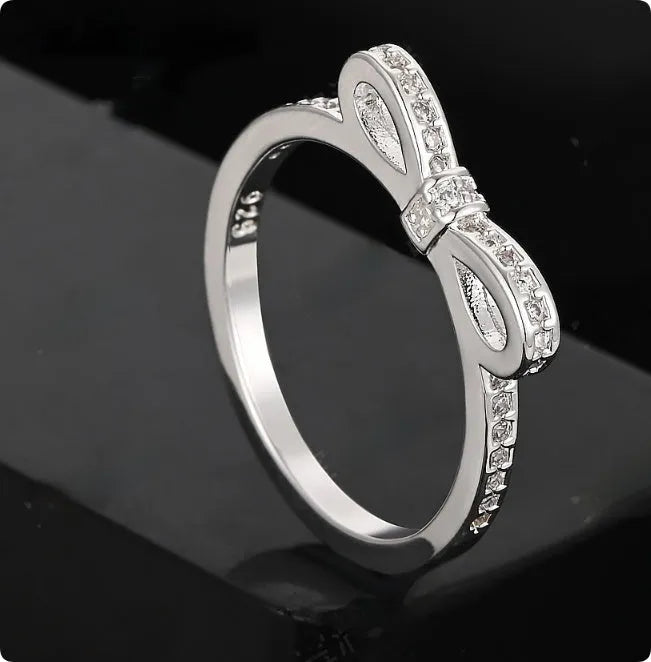 Silver bow-shaped ring with zircon crystal accents on finger, showing electroplated finish and detailed bow design