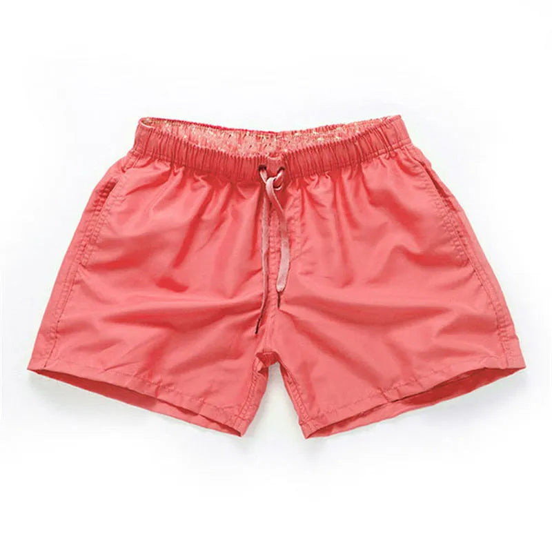 Man wearing straight-leg polyester beach shorts in a bright colour on the sand.