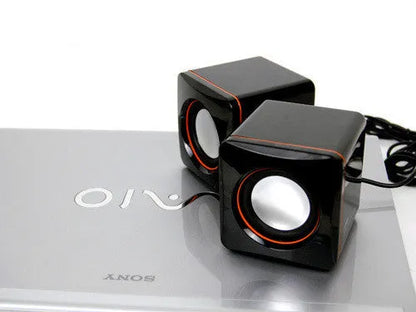 Black square USB computer speaker measuring 10cm with matte finish beside monitor