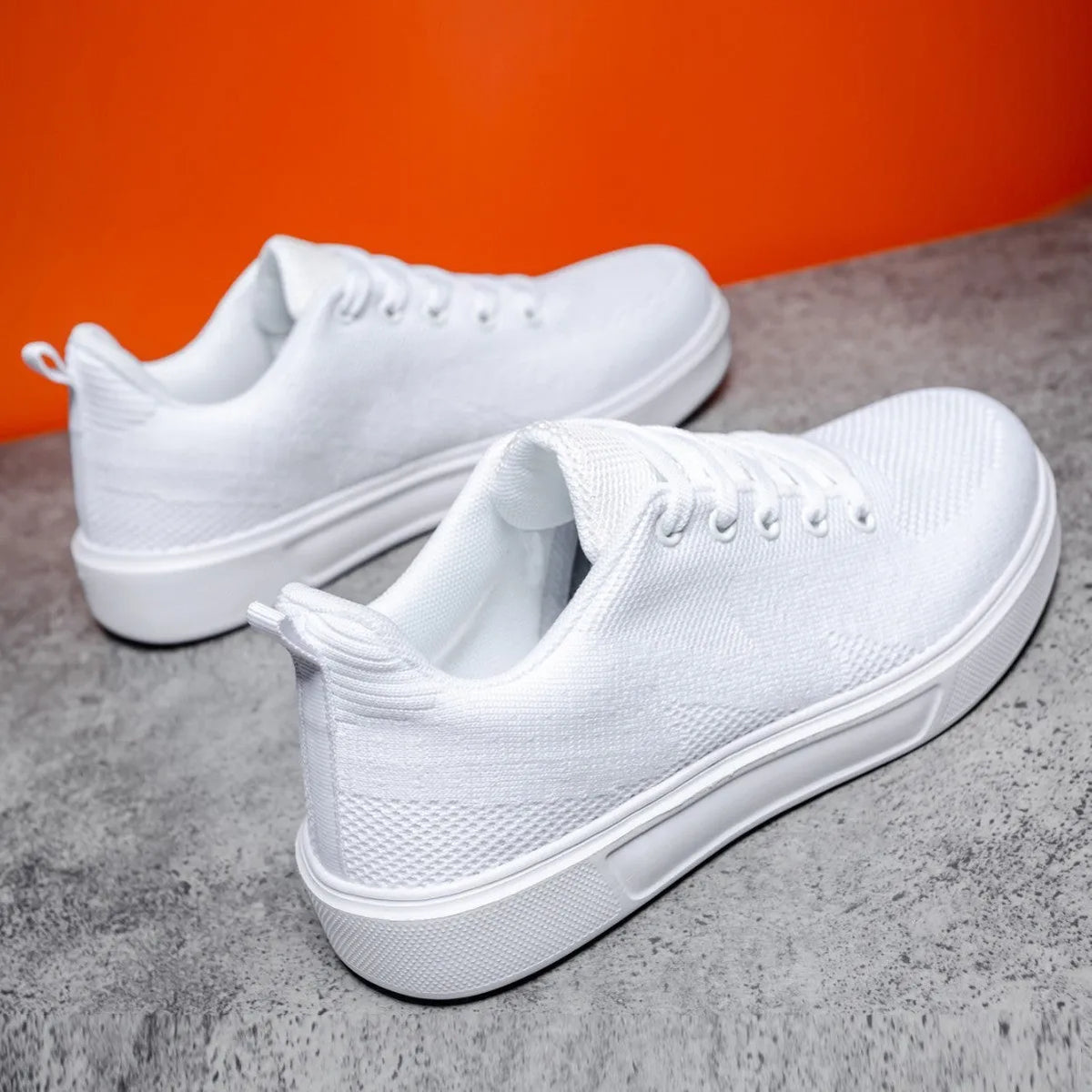 Pair of light white thick-soled casual sneakers with mesh upper and lace-up front.