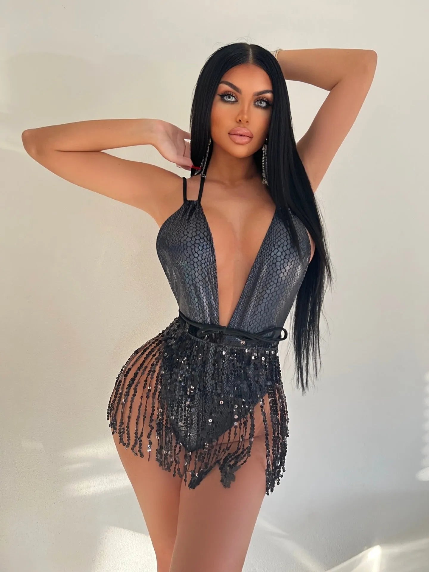 Gold backless one-piece swimsuit with tassel detailing on a solid colour background.