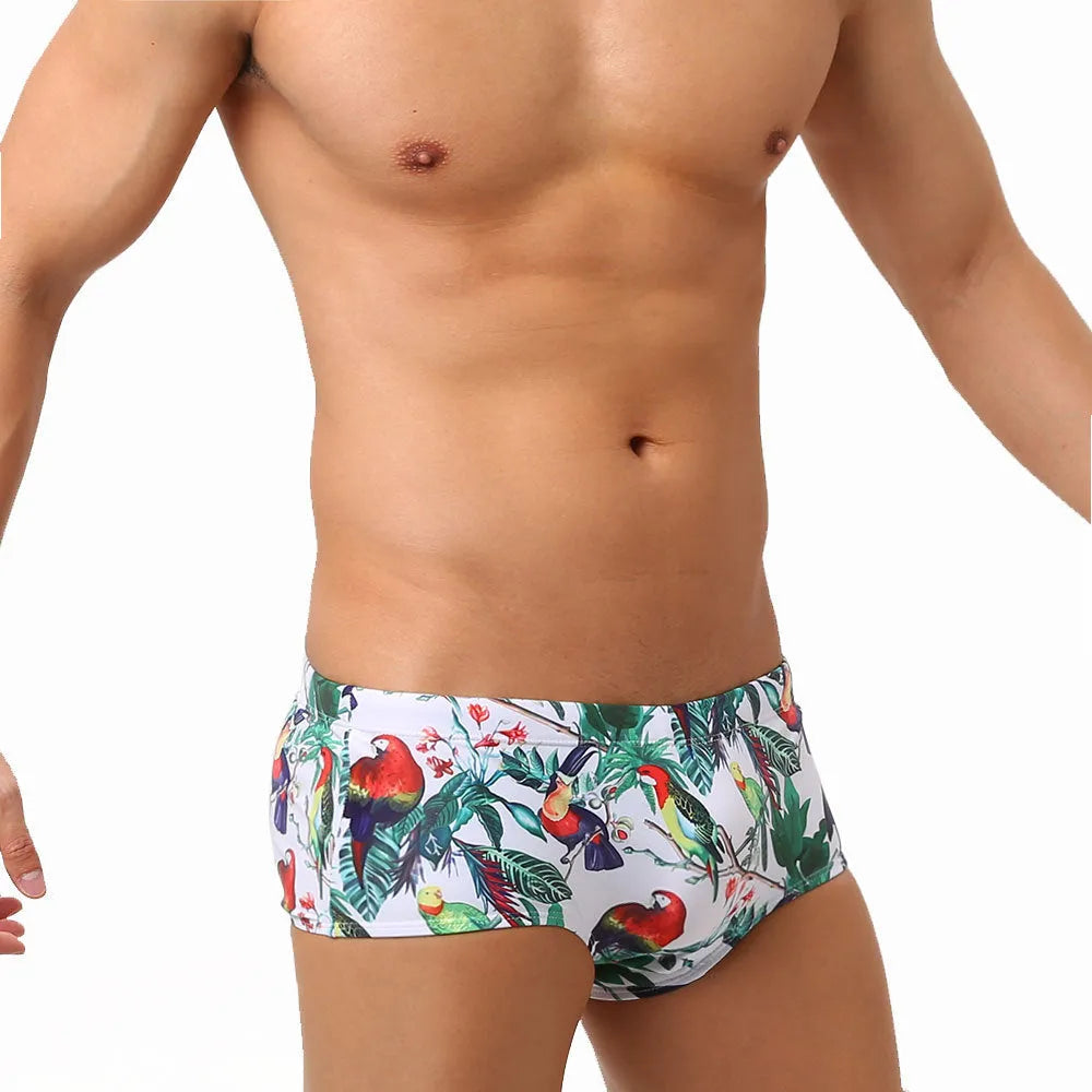 Men's blue swimming trunks with a detailed floral and bird print pattern, shown in a brief style.