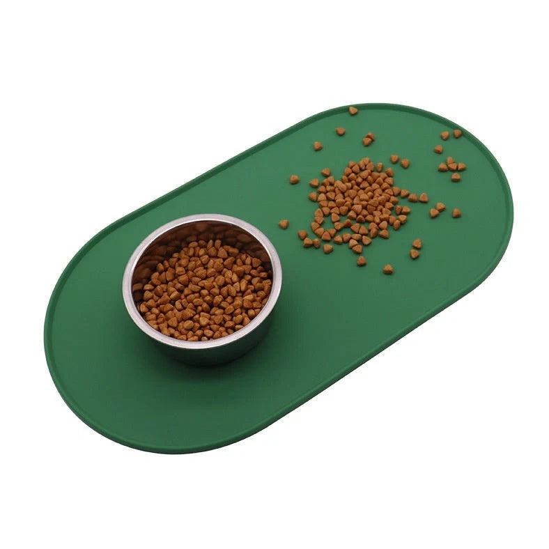 Green silicone cat feeding placemat with raised edges on wooden floor containing water bowl
