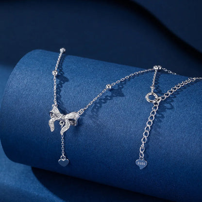 Close-up of a silver heart and bow pendant on an adjustable O-ring chain, resting on a collarbone.