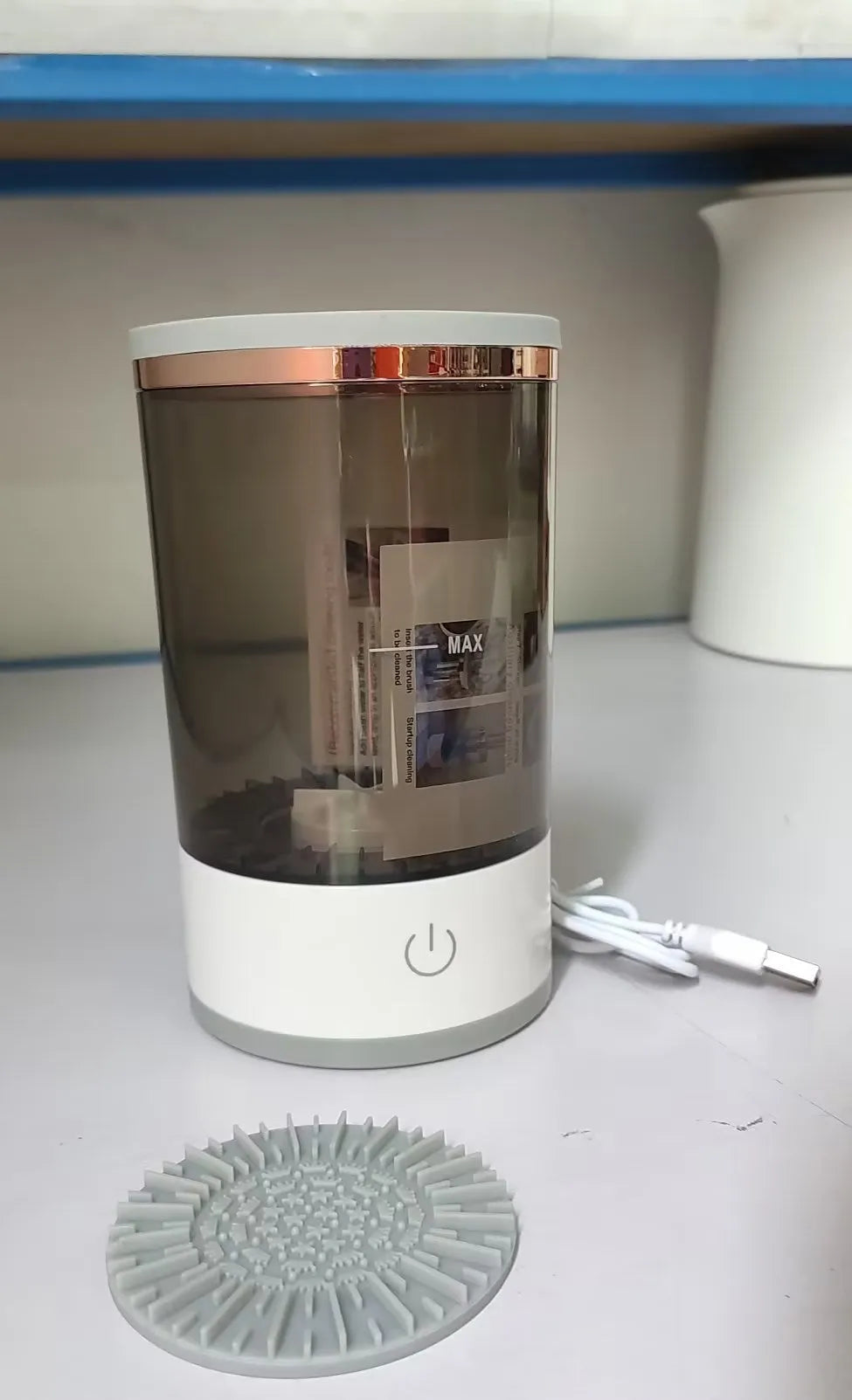 Grey and white portable electric makeup brush cleaner with USB charging cable.