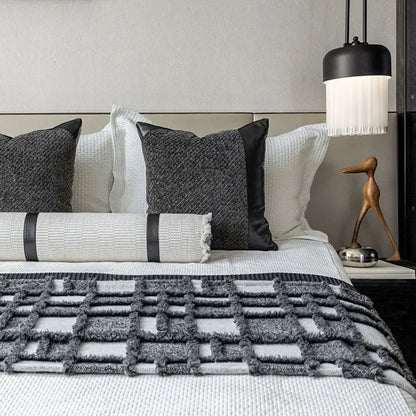 Grey and white plaid bed runner blanket with coordinating pillowcase and round leather pillow on bed
