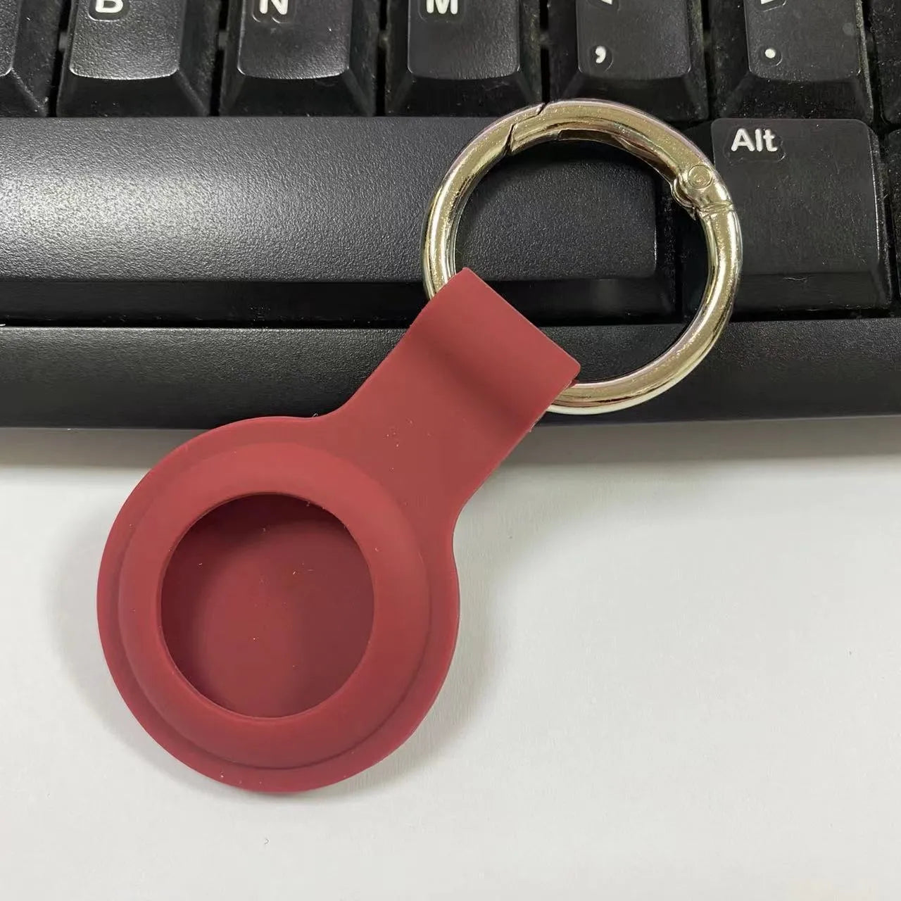 Black waterproof silicone Airtag protective case with metal keychain clip, shown next to colour options.