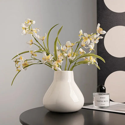 Black ceramic vase with round belly design and two white artificial orchid stems on wooden table