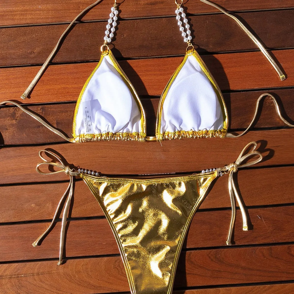 Gold women's halter neck bikini with lace-up front and pearl chain decoration on a solid background.