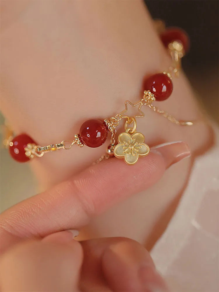 Red agate double layer bracelet with flower and peach blossom charms on a wrist.