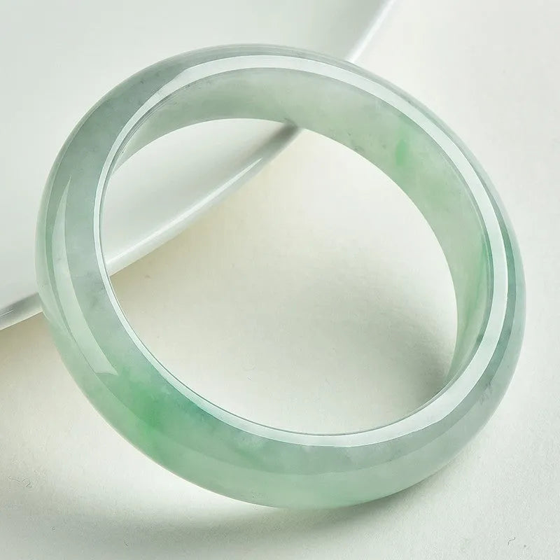 Light green solid jade bracelet on a wrist, showing its simple loop design and natural stone colour.