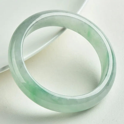 Light green solid jade bracelet on a wrist, showing its simple loop design and natural stone colour.