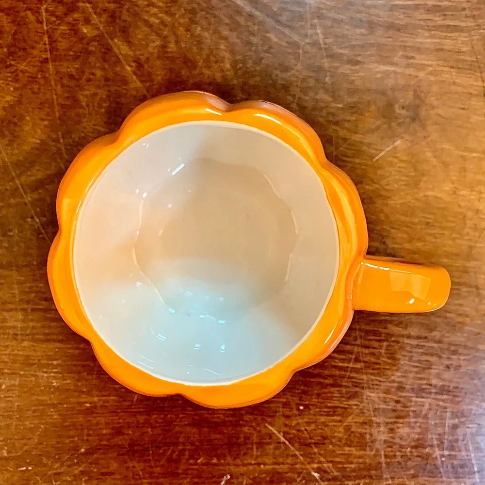 Orange ceramic Halloween pumpkin mug with cartoon face and included spoon on autumn table