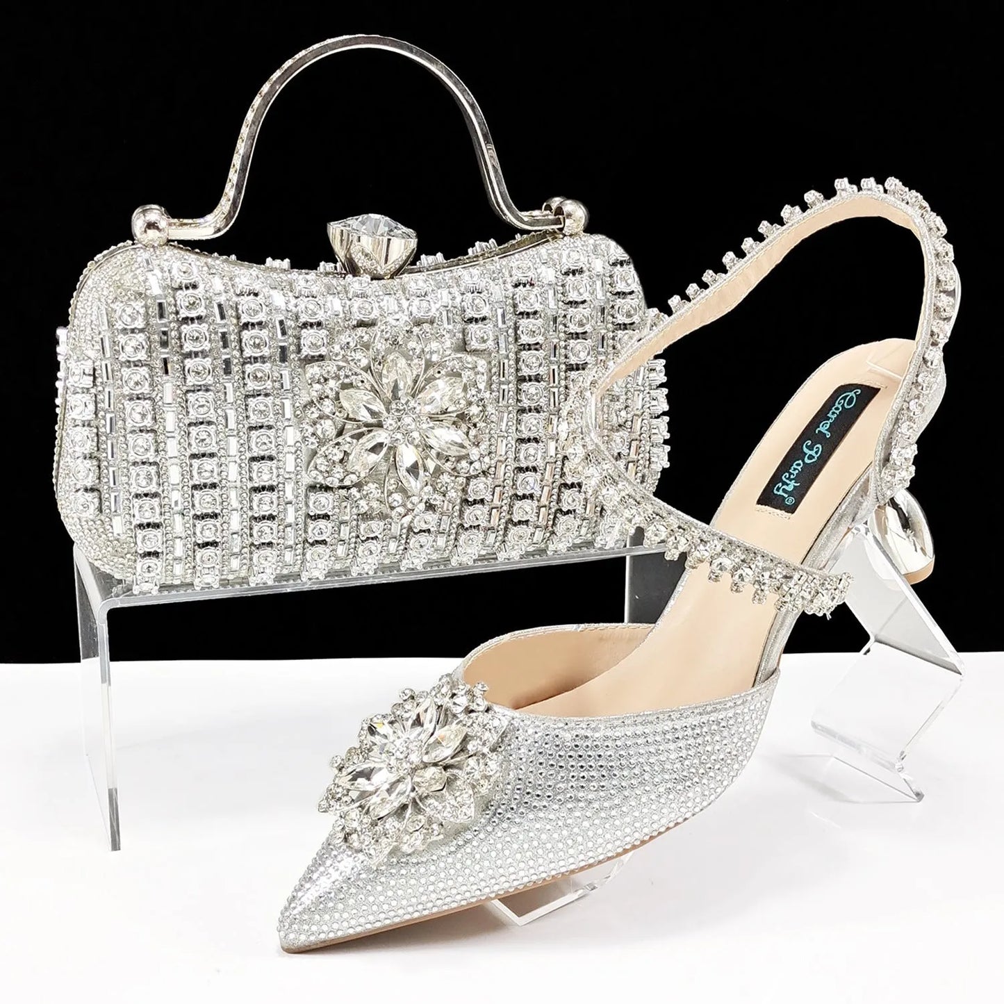 Women's black high-heel ankle strap shoes with floral rhinestone buckle and matching clutch bag on a neutral background