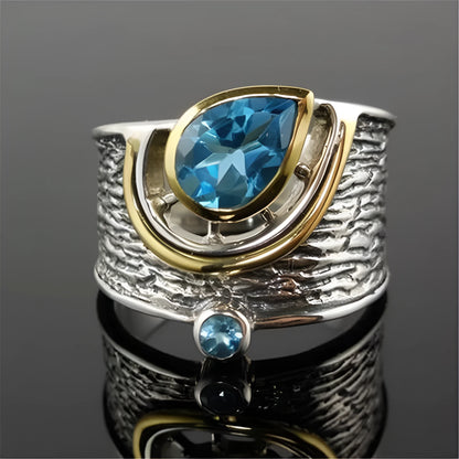 Close-up of a blue zircon drop-shaped alloy ring on a woman's finger, showing the inlaid stone setting.
