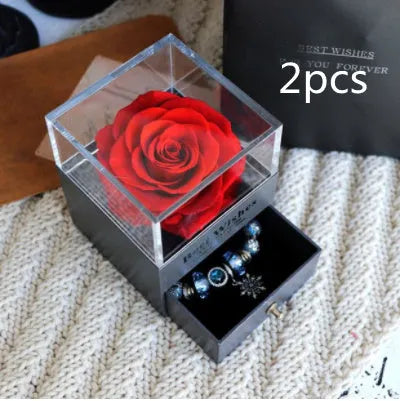 Blue and pink eternal flower gift box with roses and carnations on a table.