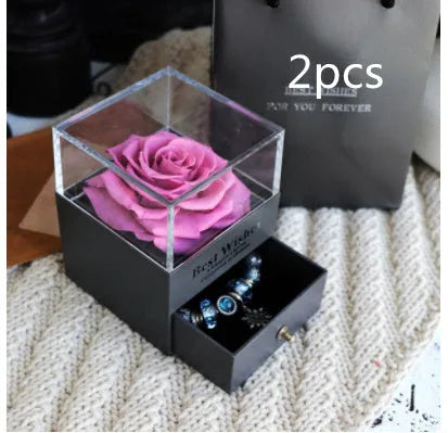 Blue and pink eternal flower gift box with roses and carnations on a table.