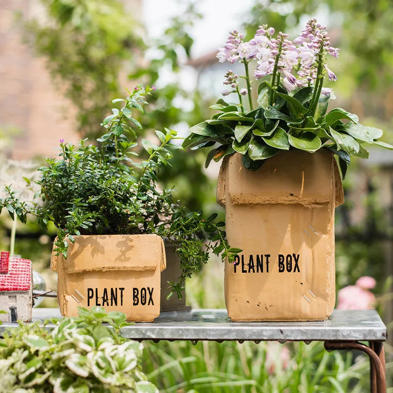 Square cement planter with matte finish and drainage holes, next to a small green plant.