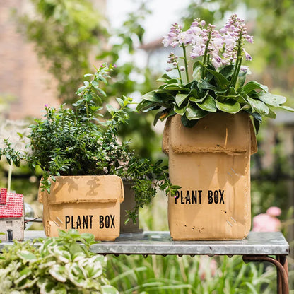 Square cement planter with matte finish and drainage holes, next to a small green plant.