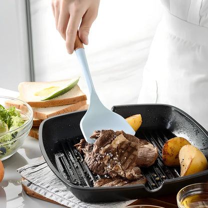 Blue silicone non-stick cookware set with frying spatula, colander, egg beater, and white iron storage bucket for kitchen organisation