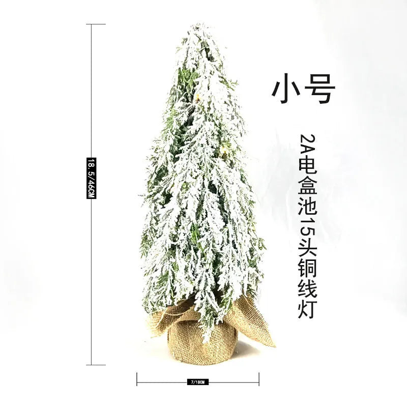Small green artificial Christmas tree with white snowy branches and built-in warm white lights on a desktop.