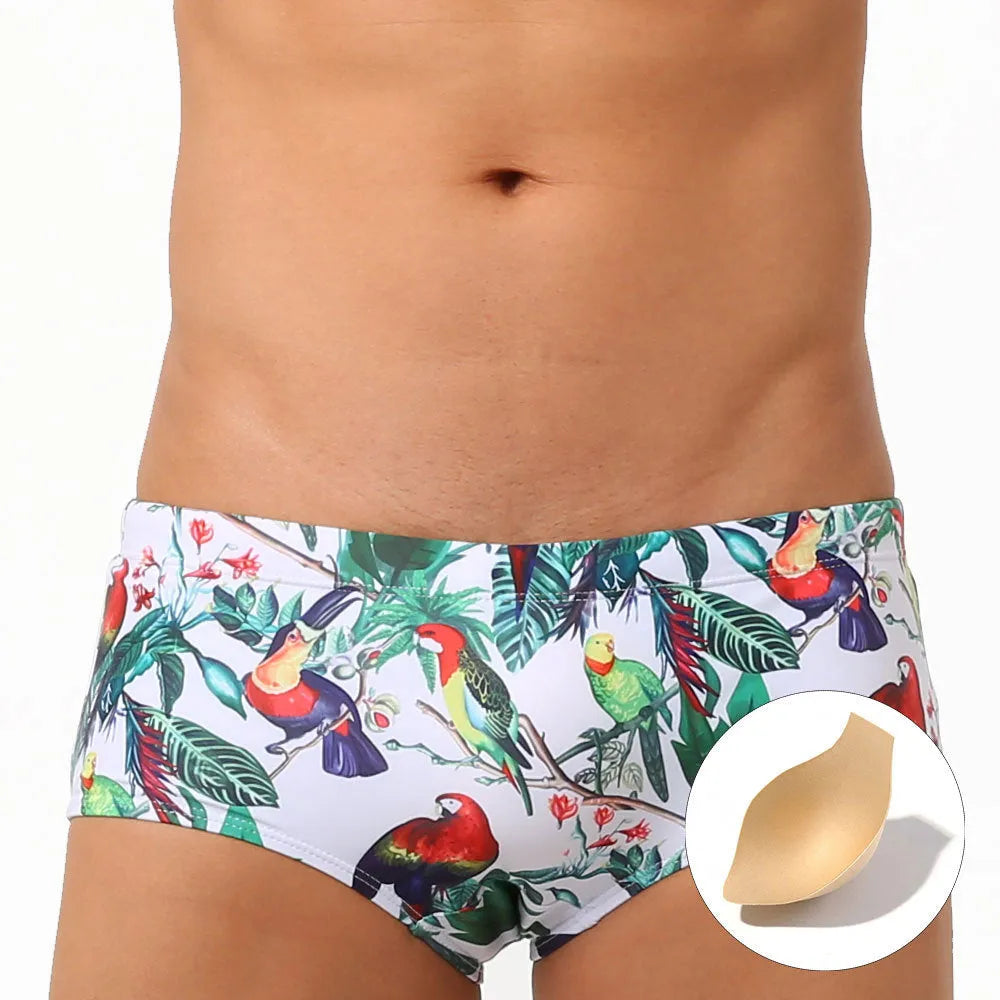 Men's blue swimming trunks with a detailed floral and bird print pattern, shown in a brief style.