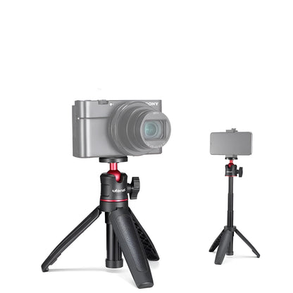 Compact black red and white phone tripod selfie stick stand extended next to a mobile phone.