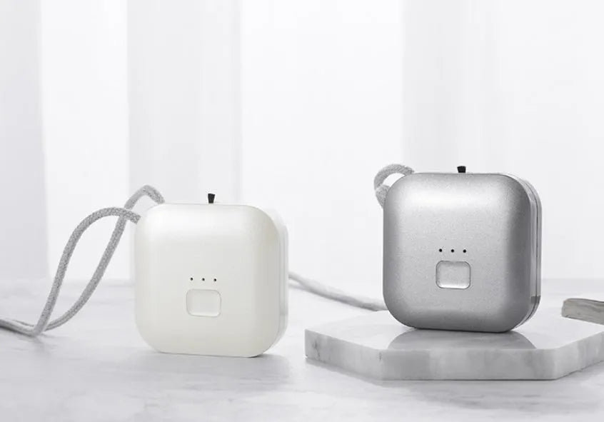 Pink wearable USB air purifier necklace on a table with USB cable, showing compact size.