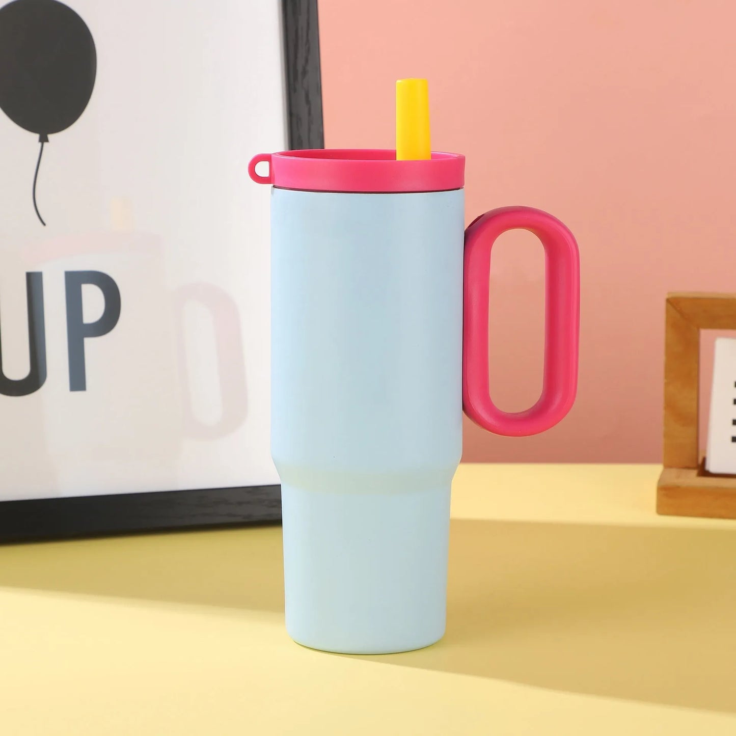 Large pink insulated straw cup with a black handle and push-button lid on a wooden table