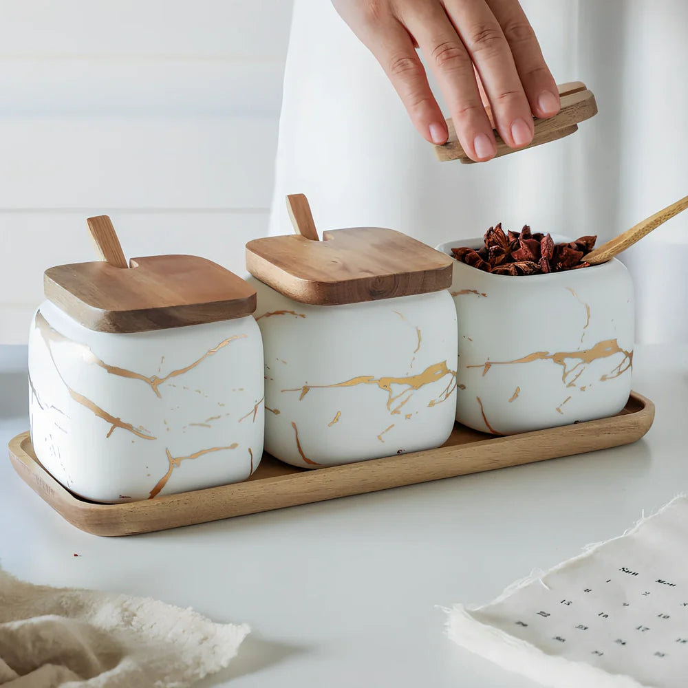Three-piece Nordic Gold Marble Jar Set in white ceramic with wooden tray and bamboo spoons on kitchen counter