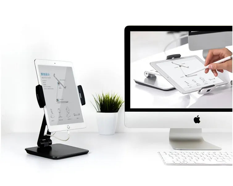 Silver foldable aluminium phone and tablet holder on a wooden desk, showing 360-degree rotation and silicone pads.