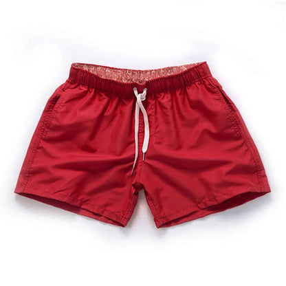 Man wearing straight-leg polyester beach shorts in a bright colour on the sand.