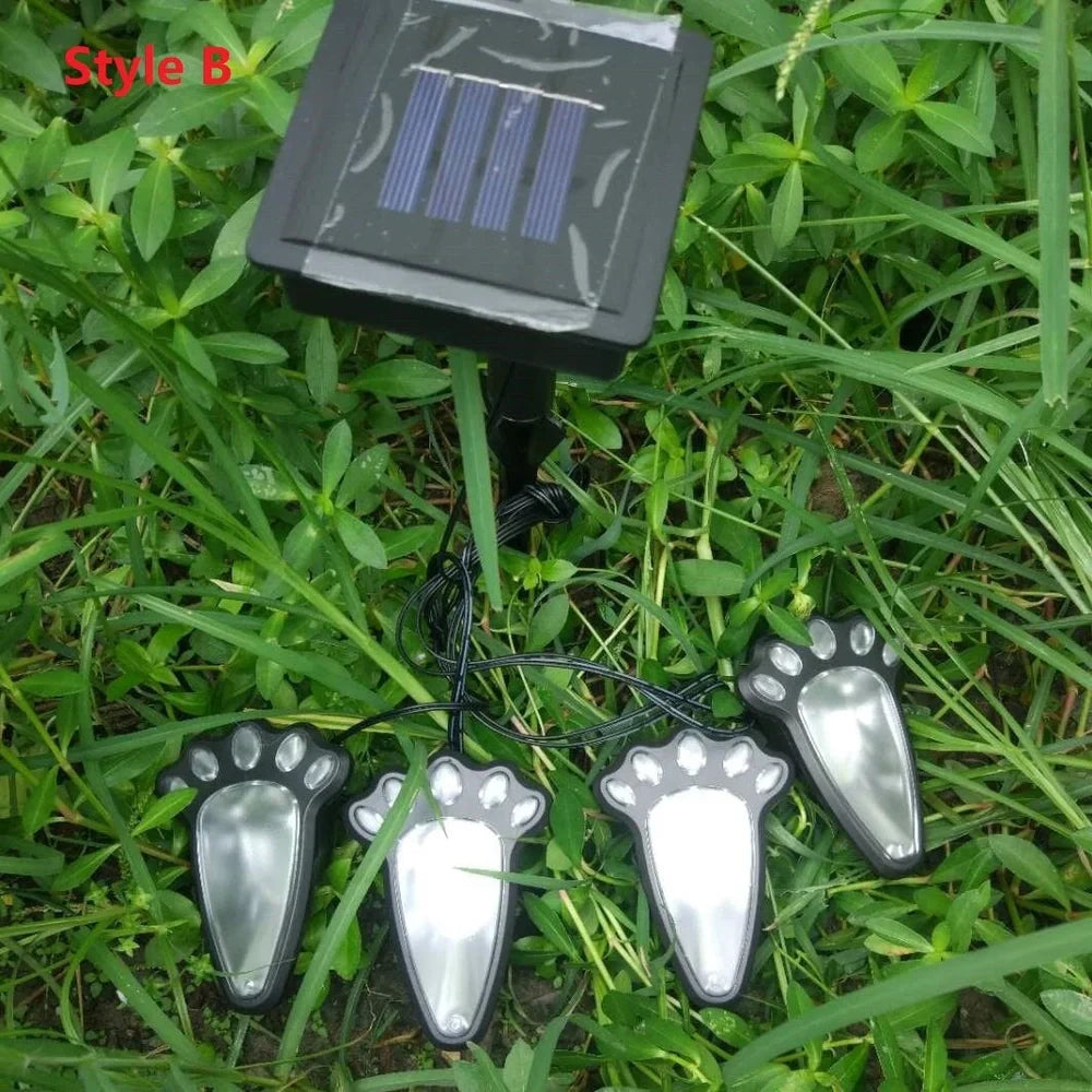 Four black paw-shaped solar garden lights with connecting wire and central solar panel for automatic outdoor illumination