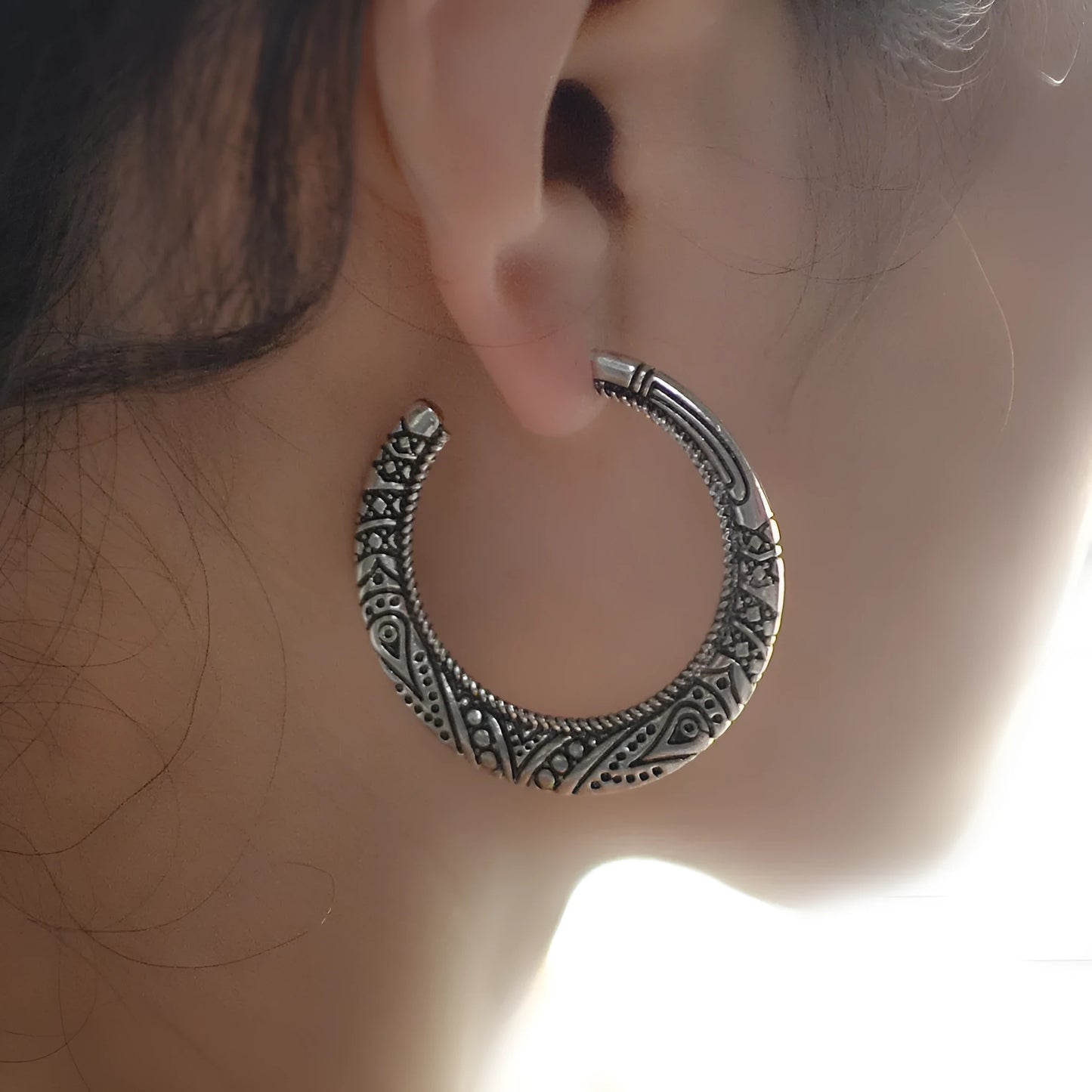 Close-up of vintage-style C-shaped alloy earrings with engraved detail, shown in bronze tone.