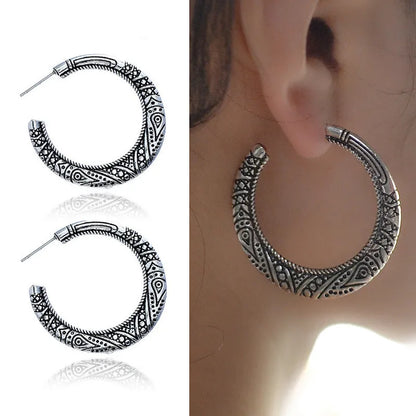 Close-up of vintage-style C-shaped alloy earrings with engraved detail, shown in bronze tone.