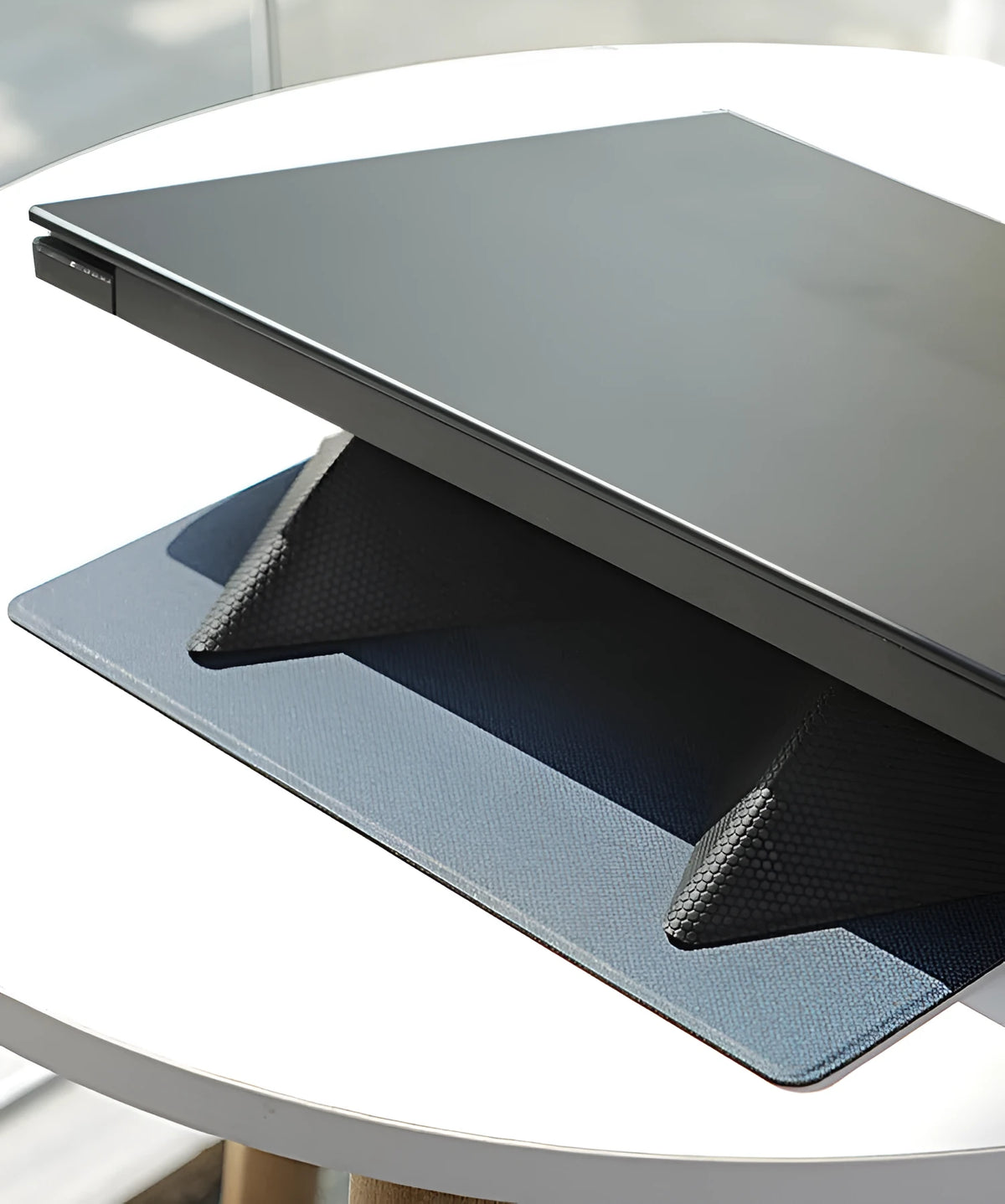 Blue or grey foldable laptop cooling stand with anti-slip surface on a desk.