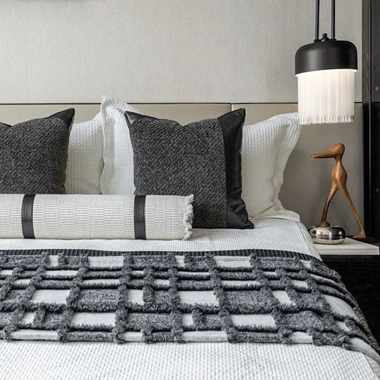 Grey and white plaid bed runner blanket with coordinating pillowcase and round leather pillow on bed
