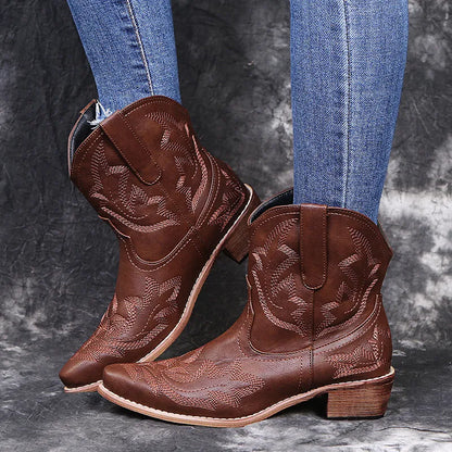 Blue women's cowboy ankle boots with white embroidery and a low wedge heel on a wooden floor.