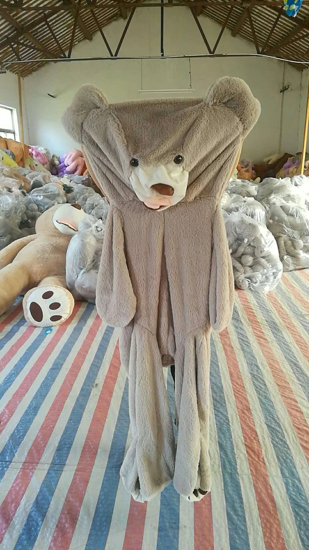 A giant, plush teddy bear in a variety of sizes and colors, including light brown, dark brown, gray, white, pink, and purple.