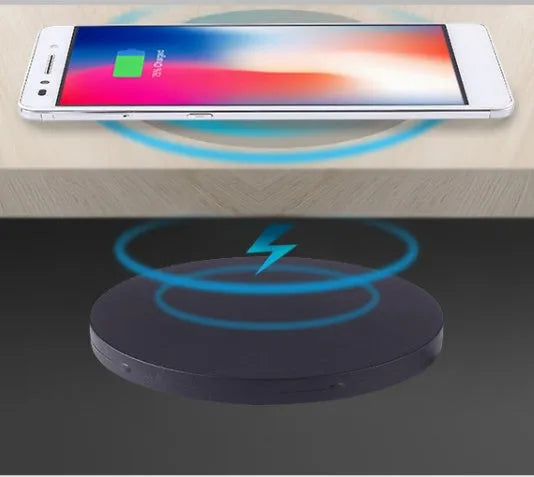 Round wireless charging unit for recessed installation in desks and tables, shown next to a smartphone.