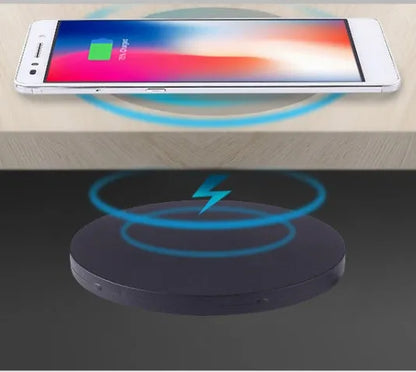 Round wireless charging unit for recessed installation in desks and tables, shown next to a smartphone.