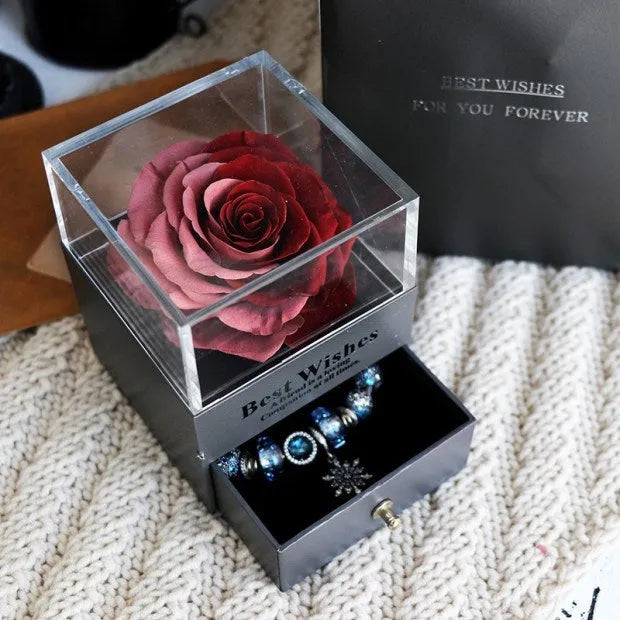 Blue and pink eternal flower gift box with roses and carnations on a table.