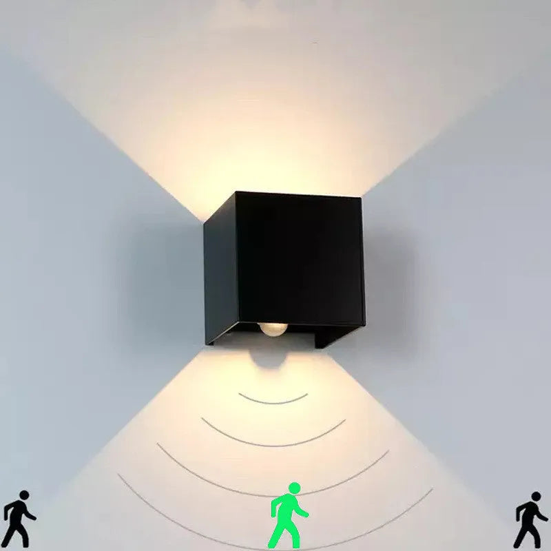 Modern cubic wall lamp in black finish mounted on a corridor wall, emitting a warm white light.