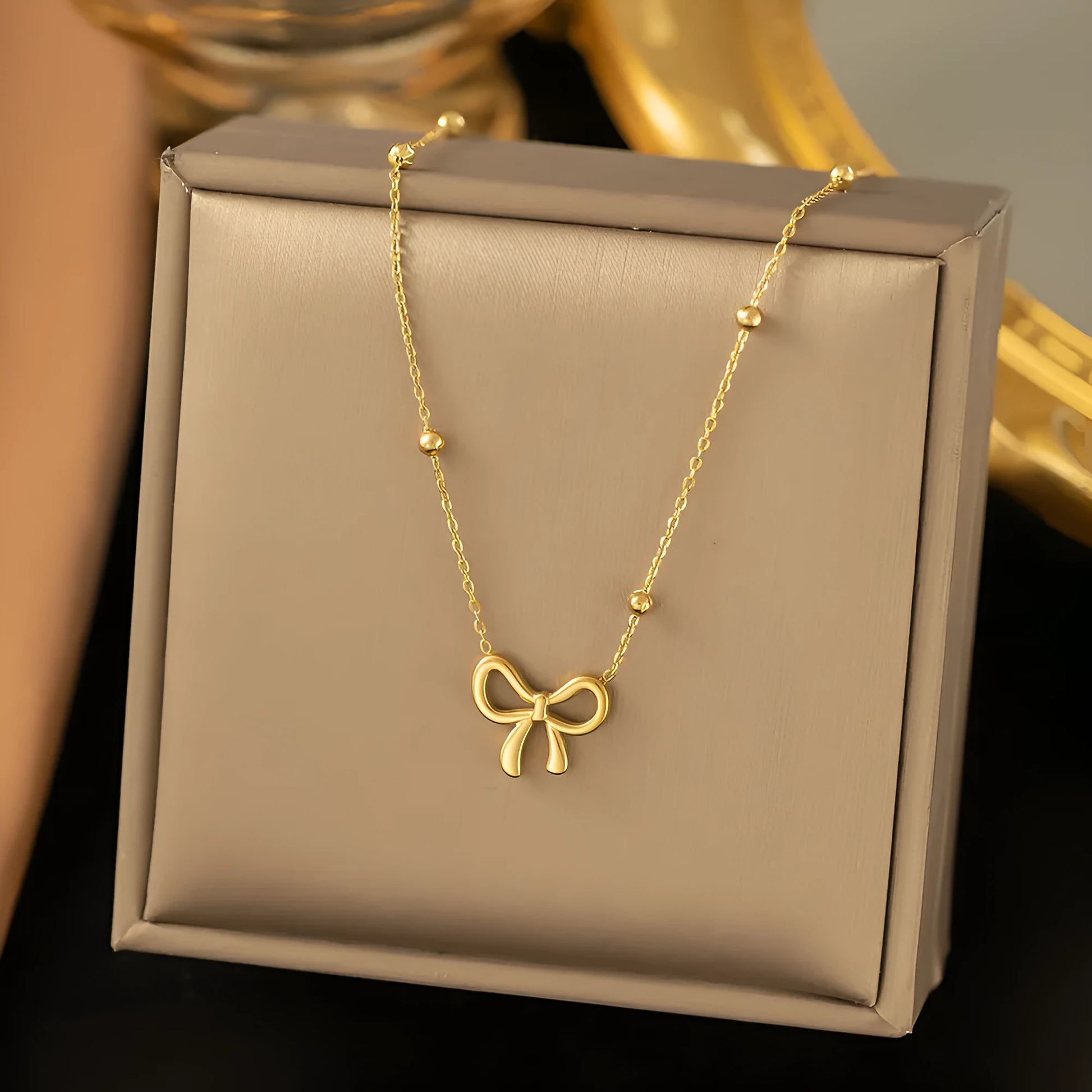 Gold titanium steel necklace with bow pendant on an adjustable cross chain, length 41cm to 50cm.