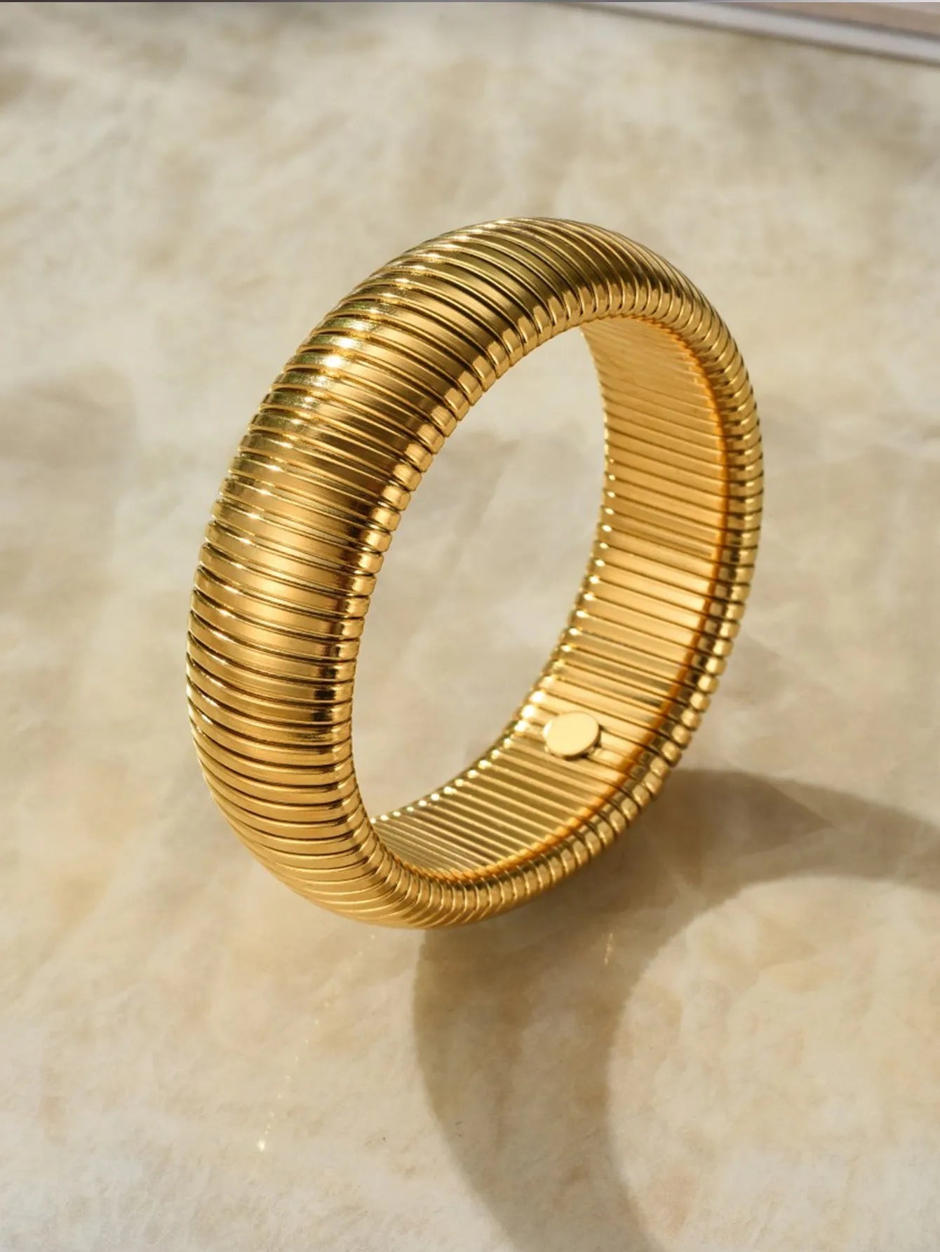 Women's titanium steel elastic bracelet with a vertical stripe pattern in gold, shown on a wrist.