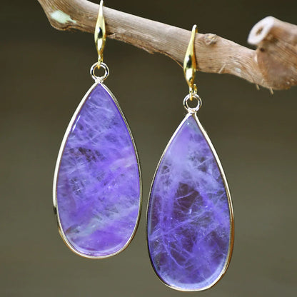 Close-up of long, polished tigereye stone drop earrings with a fishhook clasp on a neutral background.